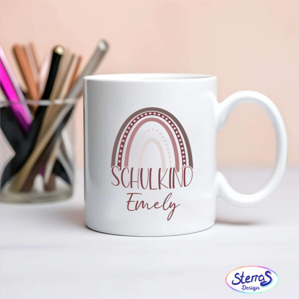 Weiße Tasse mit dem Design in Brauntönen. Unter dem Wort „Schulkind“ steht der Name „Emily“. Links neben der Tasse befindet sich ein Glas mit bunten Stiften.