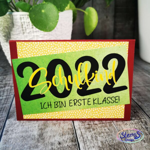 DIY-Schriftzug „2023 – Ich bin erstklassig“ in Schwarz-Gelb auf Kartenhintergrund. Präsentiert mit bunter Einschulungstüte – persönliche Dekoidee zur Einschulung.