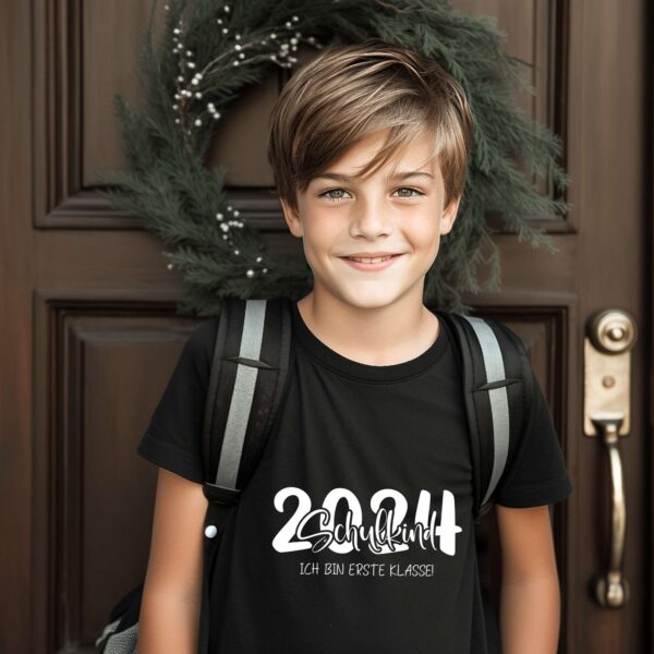 Junge mit Schulranzen trägt schwarzes Shirt mit weißem Aufdruck „2024 Schulkind“. Vor Haustür mit Ranzen – modernes Mockup für Einschulungsdesigns.