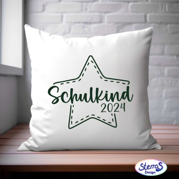 Weißes Kissen mit dunkelgrünem Design; Schulkind 2024 mit einem Sternenrahmen. Das Kissen steht vor einer rustikalen weißen Wand auf einem Holztisch.