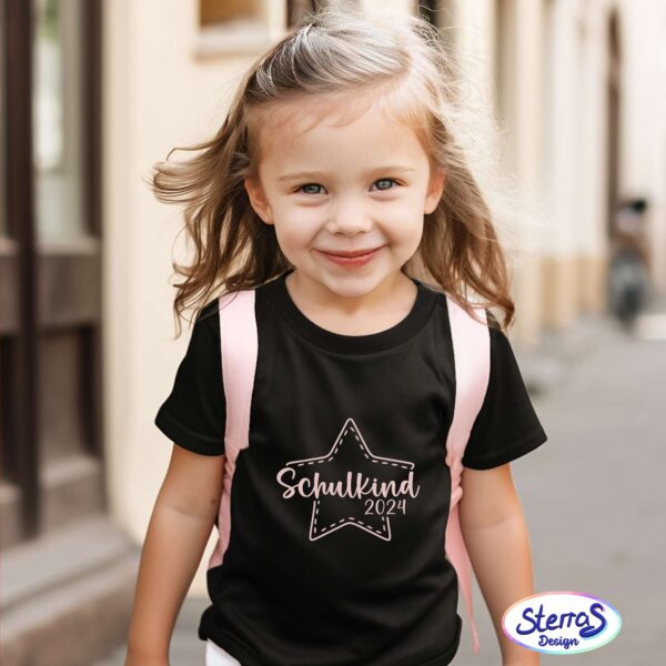Mädchen trägt schwarzes T-Shirt mit weißem Aufdruck „Schulkind 2024“ in Sternform, fröhlich draußen unterwegs – Mockup für Schuleinschulung.
