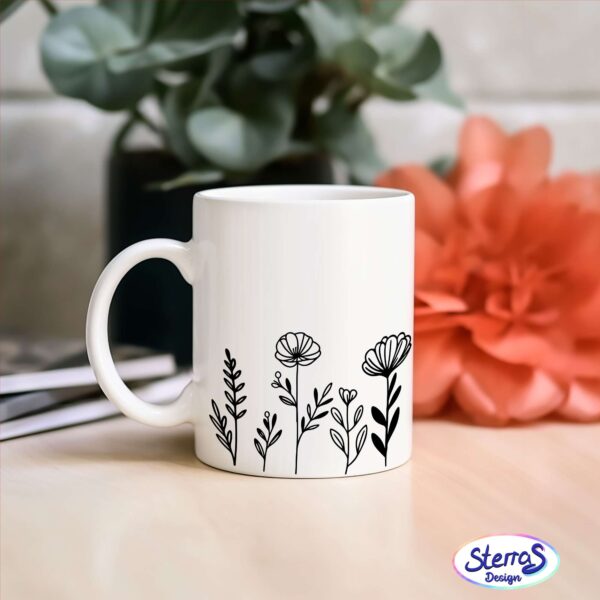 Weiße Keramiktasse mit zartem floralen Blumenwiesen-Motiv, daneben eine rote Blume, perfekt als Geschenk für Natur- oder Gartenliebhaber.