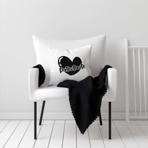 Das Herzdesign in Schwarz auf einem weißen Kissen, das auf einem weißen Stuhl liegt. Der Stuhl ist mit einer kuscheligen schwarzen Decke dekoriert – gemütlicher Look.