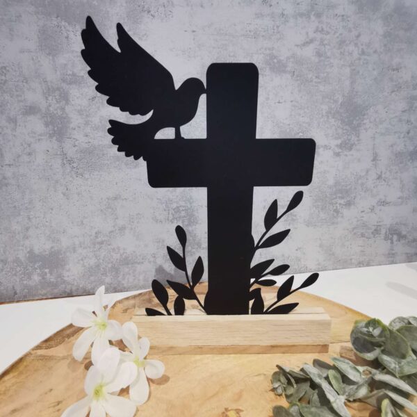 Beispielanwendung der Datei „Kreuz Blumen“: Zu sehen ist die Datei ausgeschnitten aus dicken schwarzem Karton und mithilfe von Klötzchen hingestellt. Die Deko steht auf einem Holzteller vor einem hellgrauen Hintergrund und ist dekoriert mit Blumen.