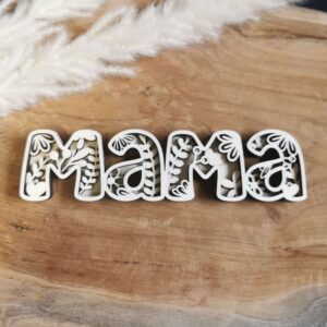 Schriftzug „Mama“ aus Papier oder Holz mit floraler Konturschicht, darunter dunkle Grundschicht. Liegt auf hellem Holz – elegante Handarbeit mit Tiefe durch Lagen-Look.