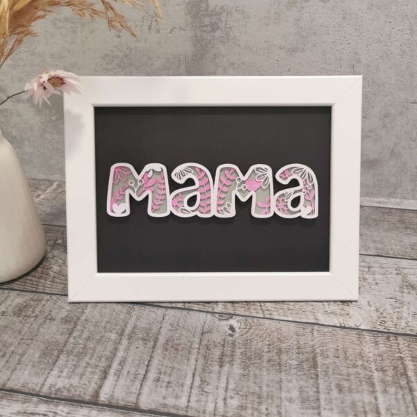 Gerahmter Schriftzug „Mama“ in rosa Tönen mit floralem Cutout-Stil. Dekorativ aufgestellt auf weißer Kommode – stilvolles Geschenk für Muttertag oder Geburtstage.