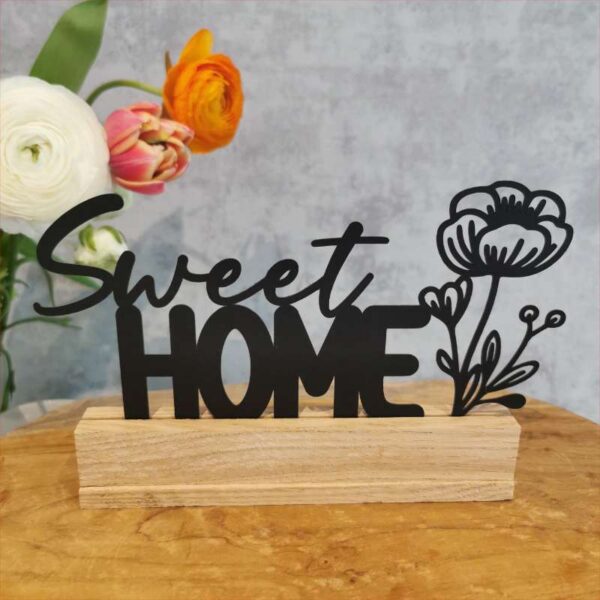 Anwendungsbeispiel der Plottdatei: „Sweet Home“ mit Blume, aus schwarzem Acryl ausgeschnitten, als Klötzchendeko auf einem Holztisch aufgestellt. Im Hintergrund eine Vase mit Blumen vor schlichtem grauen Hintergrund.