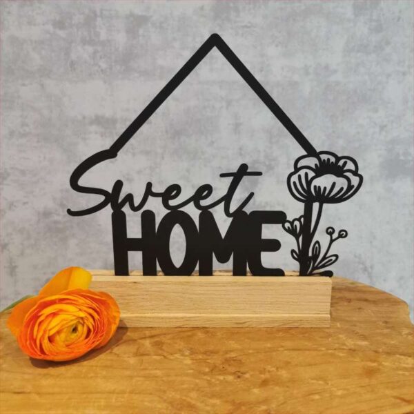 Produktbild 5 (Beispielbild – Sweet Home mit Hausdach): Die Variante der Plottdatei mit Hausdach – „Sweet Home“ mit Blume darunter – ausgeschnitten aus schwarzem Acryl, als Klötzchendeko inszeniert. Auf einem Holztisch platziert, vor neutralem Hintergrund mit dekorativer Blume im Vordergrund.