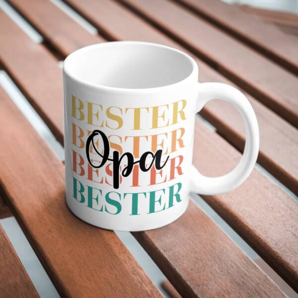 Weiße Tasse mit sublimiertem Motiv „Bester Opa“ in bunten Farben. Die Tasse steht auf einem Holztisch.