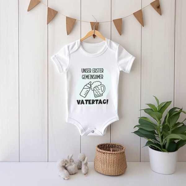 Weißer Babybody mit dem Design in hellblau und schwarz, aufgehängt an einer Girlande. Unten rechts im Bild befindet sich eine einzelne Blume. Sanftes, verspieltes Setting.
