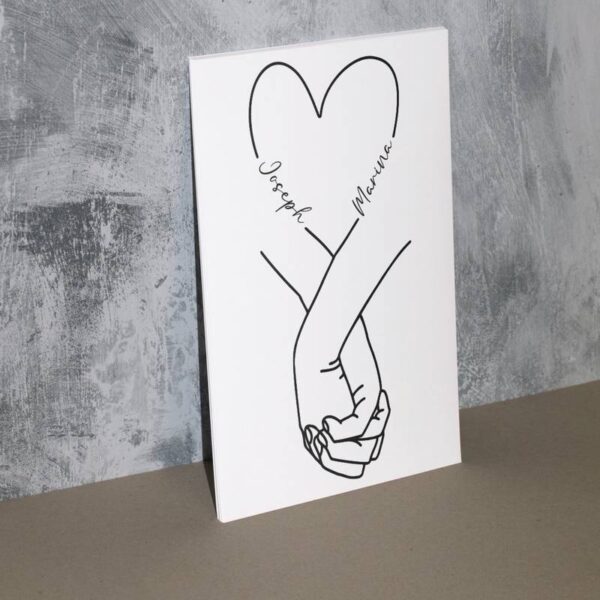 Schild mit Hand-in-Hand-Motiv und einem Herz darüber, aufgestellt auf einer grauen Oberfläche – schlicht und emotional.