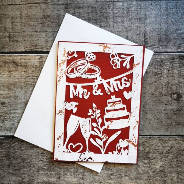 Tiefrote Karte mit weiß hinterlegten Hochzeitssymbolen (Ringe, Sektgläser, Herzen) und dem Text „Mr & Mrs“. Präsentiert mit weißem Umschlag auf Holz. Elegante DIY-Papeterie.