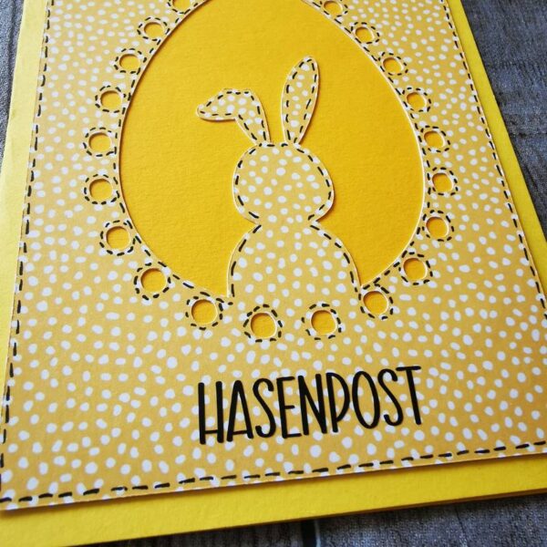 Nahaufnahme der gelben „HASENPOST“-Osterkarte mit Hasensilhouette im Ei und verspieltem Blumenhintergrund.