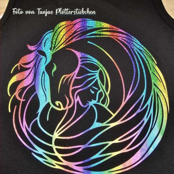 Nahaufnahme des geplotteten Motivs auf schwarzem T-Shirt, diesmal in schimmernder Regenbogenfolie. Das Motiv zeigt Mädchen und Pferd mit farbenfrohem Effekt.