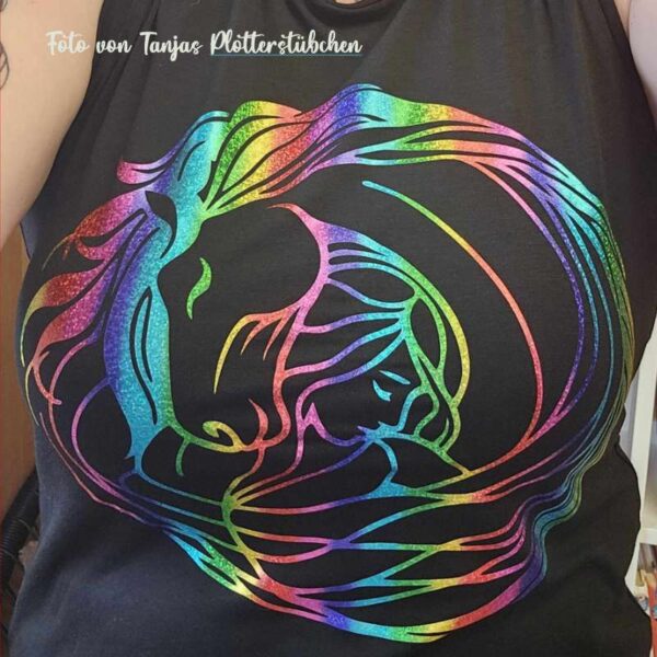 Getragenes Beispiel der geplotteten Datei auf einem schwarzen T-Shirt. Das Motiv in Regenbogenfolie wird auf Brusthöhe präsentiert, die Aufnahme zeigt den Oberkörper ohne Kopf für Fokus auf das Design.