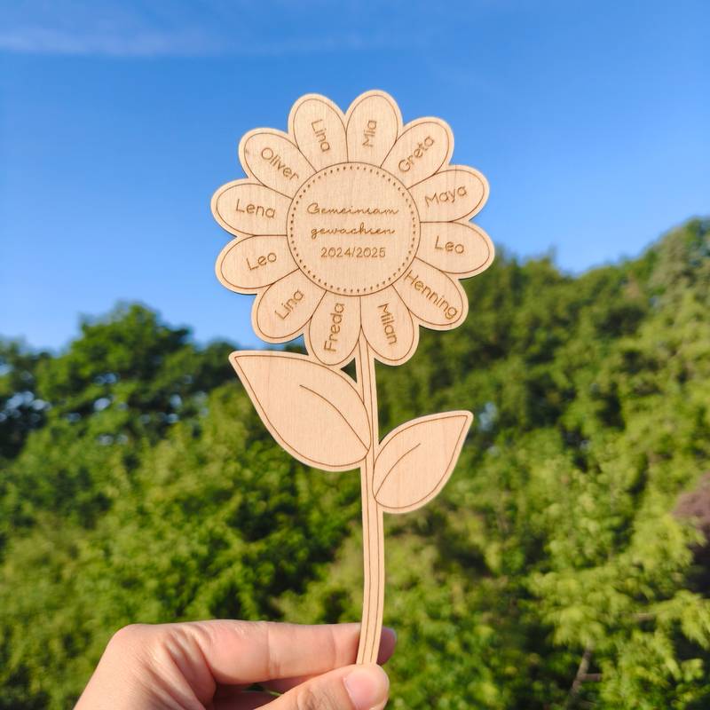 Eine Hand hält eine personalisierte Holz-Sonnenblume. In den Blütenblättern sind Namen von Kindern eingraviert.