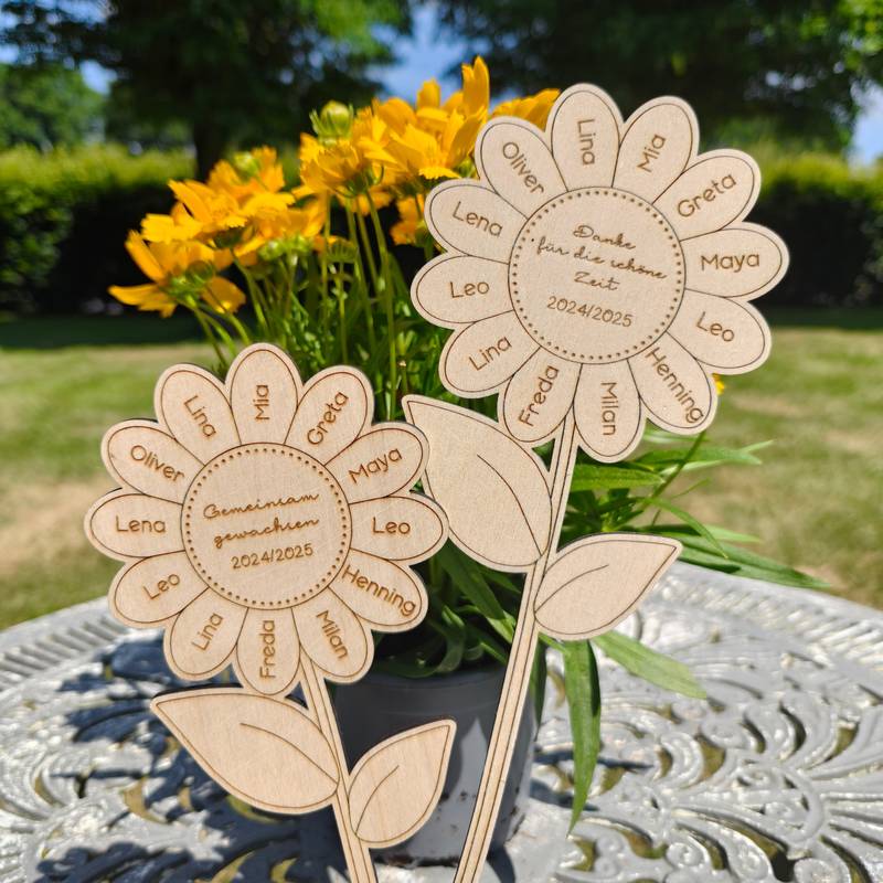Zwei lasergeschnittene Sonnenblumen aus hellem Holz stehen in einem Blumentopf im Garten.